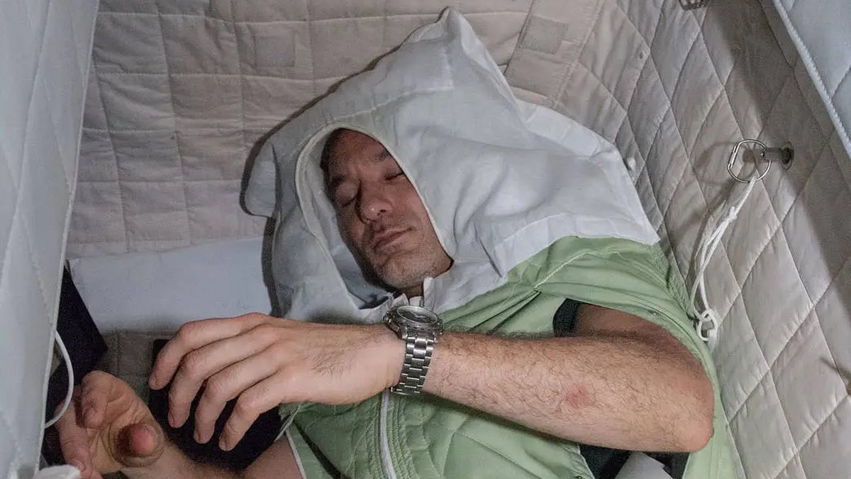 An International Space Station crew member asleep in a sleep restraint in his crew quarters
